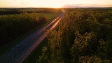 车辆在<strong>光芒四射</strong>的高速公路上行驶，日落时被树木环绕。乡村公路上的交通流量少。在高速公路上行驶的卡车和汽车，经过美丽的绿树成荫的风景.